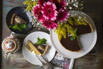 Шоколадный пирог Ganache на торте и ломтик на тарелке украшены вазой цветов и винтажный чайник на столе — стоковое фото