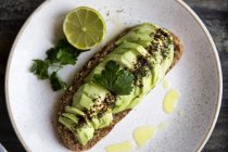 Plate of avocado toast with sauce, halved lime and herbs — Stock Photo