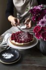 Vue partielle des mains féminines saupoudrer de sucre glace sur le gâteau à la cardamome avec des framboises — Photo de stock