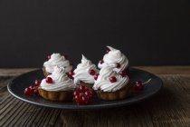 Close up of freshly baked cupcakes decorated with red currants on plate — Stock Photo