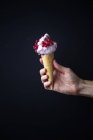 Main féminine tenant de la crème glacée avec des groseilles rouges sur le dessus sur fond noir — Photo de stock