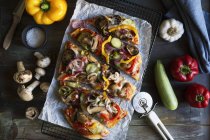 Верхний вид вегетарианской пиццы на стойке охлаждения с овощами на столе — стоковое фото