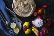 Tarta de merengue de limón en el estante de enfriamiento con limones y florero de flores - foto de stock