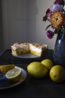 Tarta de merengue de limón en el estante de enfriamiento con limones y florero de flores - foto de stock