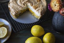 Lemon meringue pie on cooling rack with lemons and vase of flowers — Stock Photo