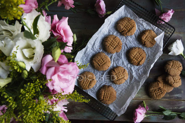 Top view of peanut butter cookies on cooling rack with flowers decoration on table — Stock Photo