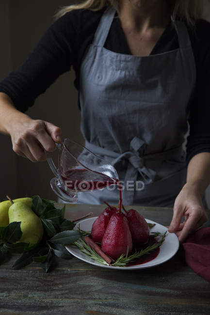 Частковий вигляд жінки, що поливає прянощі червоне вино, відбиті груші — стокове фото