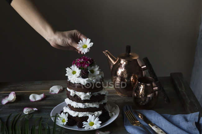 Frauen Hand verzieren Schicht Kuchen mit Gänseblümchen auf der Oberseite — Stockfoto