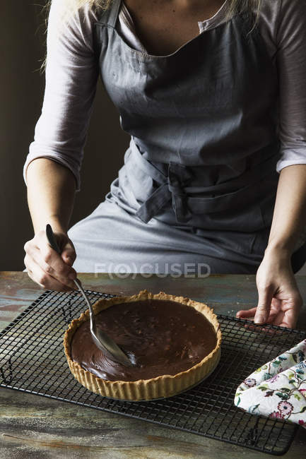 Partial view of woman pouring chocolate for Ganache Tart on cooling rack — Stock Photo