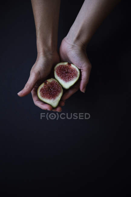 Female hands holding halved fig in hands against black background — Stock Photo