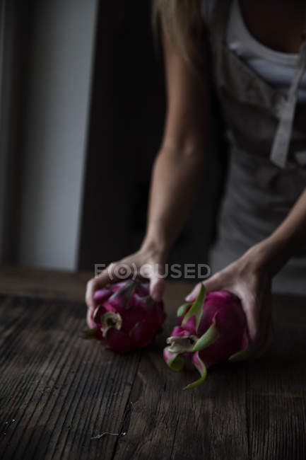 Cropped image of woman holding dragonfruits in hands on wooden table — Stock Photo