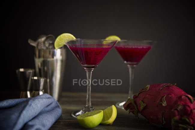 Glasses of dragonfruit cocktails with lime slices served on wooden table — Stock Photo
