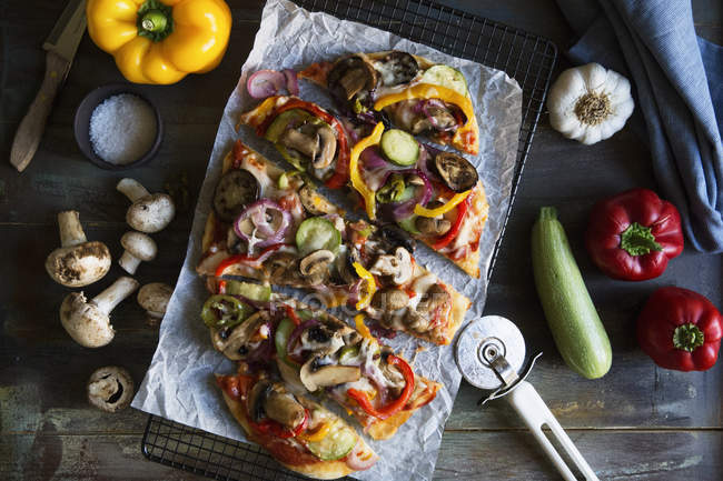 Top view of veggie pizza on cooling rack with vegetables on table — Stock Photo