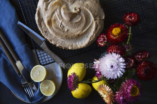 Лимонное безе пирог на охлаждающей стойке с лимонами и вазой цветов — стоковое фото