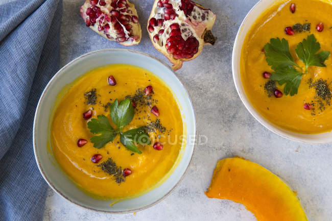 Top view of bowls of pumpkin soup with pomegranate seeds on marble surface — Stock Photo