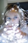 Adorable fille blonde aux yeux bleus portant des lumières de Noël — Photo de stock