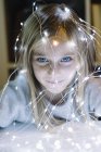 Adorable fille blonde aux yeux bleus portant des lumières de Noël — Photo de stock