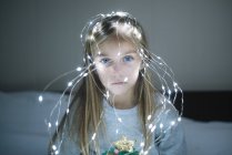 Beautiful blonde preteen girl wearing illuminated christmas garland with glowing light bulbs — Stock Photo