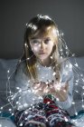 Beautiful blonde preteen girl wearing illuminated christmas garland with glowing light bulbs — Stock Photo