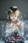 Beautiful blonde preteen girl looking at illuminated christmas garland with lights — Stock Photo