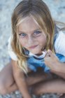 Beautiful blonde preteen girl with blue eyes sitting on floor and looking at camera — Stock Photo
