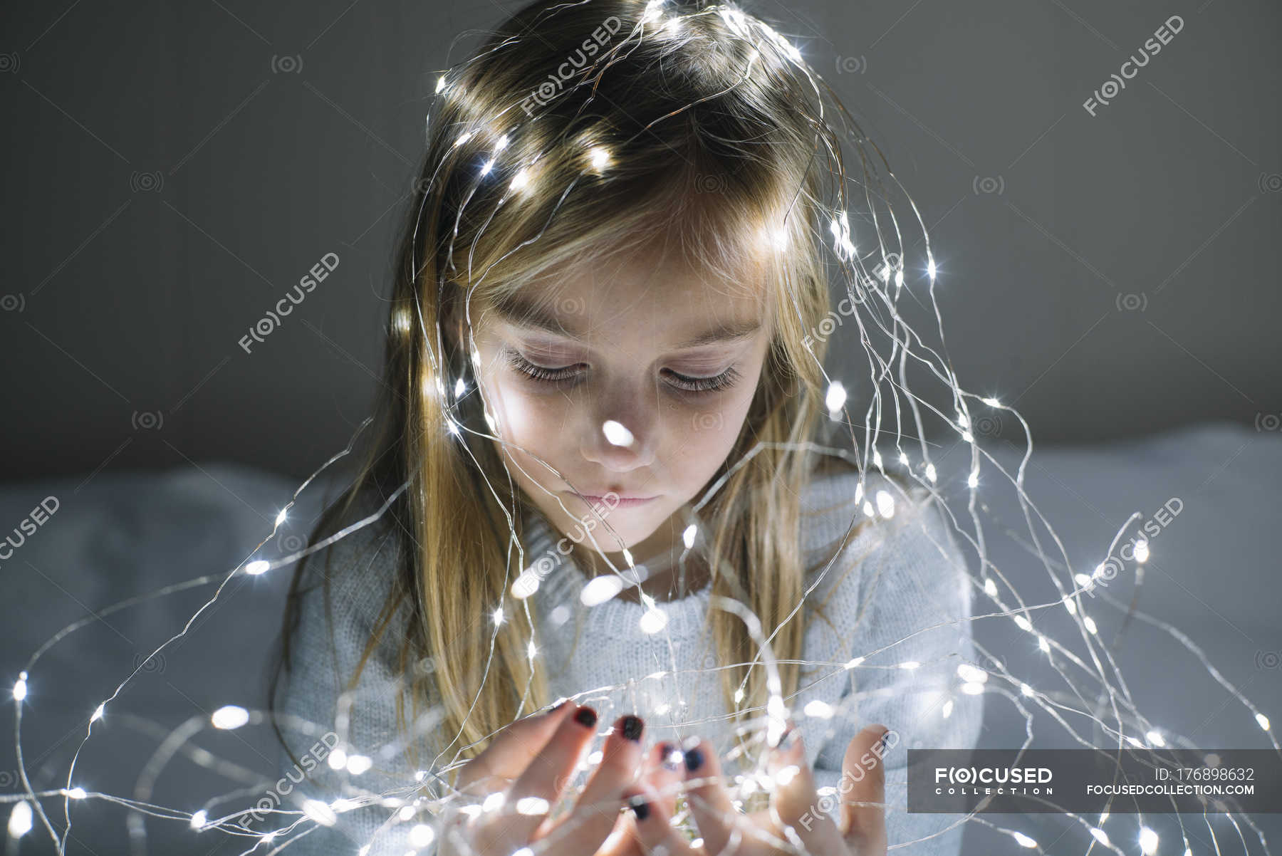 Beautiful blonde preteen girl looking at illuminated christmas garland ...