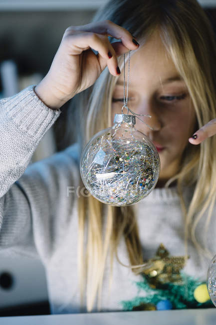 Rubia preadolescente niña sosteniendo y mirando la bola de Navidad - foto de stock