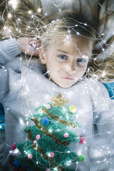 Hermosa chica rubia preadolescente con ojos azules acostado en la cama con luces de Navidad iluminadas - foto de stock