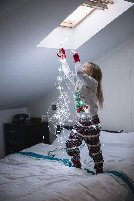 Blonde preteen girl decorating bedroom with illuminated Christmas garland — Stock Photo