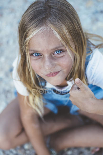 Hermosa rubia preadolescente chica con ojos azules sentado en el suelo y mirando a la cámara - foto de stock