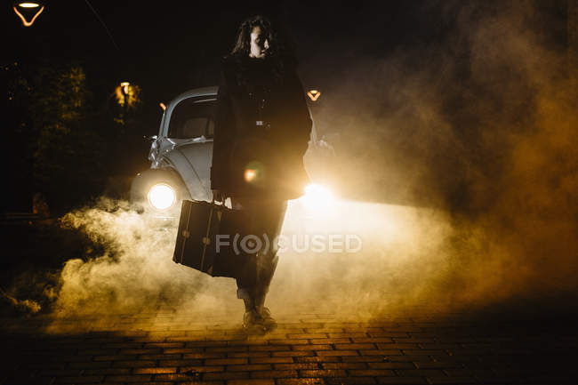 Женщин с чемоданом перед машиной с дымом — стоковое фото