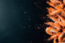 Vue de dessus du tas de crevettes sur une surface sombre avec du sel — Photo de stock