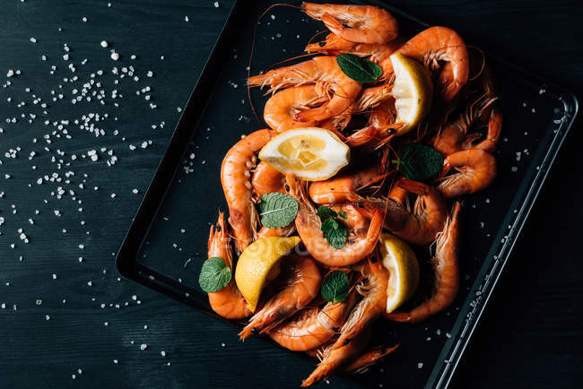 Top view of pile of shrimps with mint and lemon slices on baking tray — Stock Photo