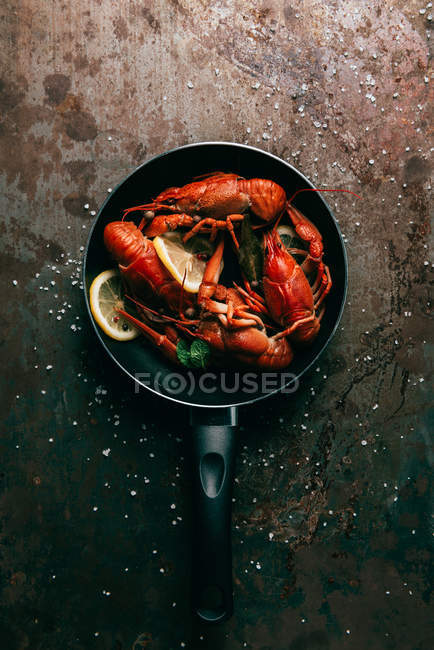 Top view of crayfishes with bay leaf, mint and lemon slices on frying pan — Stock Photo
