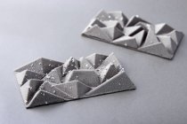 Barras de chocolate de postre de plata con patrón geométrico sobre fondo gris - foto de stock