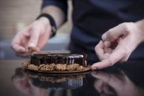 Nahaufnahme eines Konditors, der Schokoladenkuchen dekoriert — Stockfoto