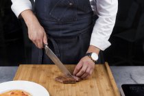 Cropped view of male chef slicing meat — Stock Photo