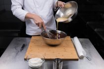 Vista recortada de la crema poring chef masculino en chocolate derretido - foto de stock