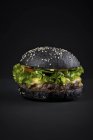 Бургер з яловичини в чорній булочці з зеленим листям салату — стокове фото