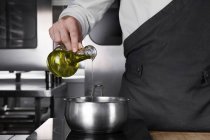 Cropped view of male chef pouring oil into pan — Stock Photo