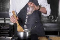 Vista recortada del chef masculino vertiendo arroz en la sartén - foto de stock