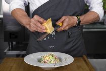 Обрезанный вид мужского сыра с решеткой шеф-повара на овощной салат — стоковое фото