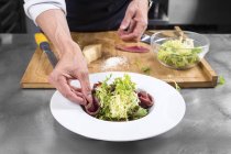 Обрезанный вид на шеф-повара, кладущего ветчину в салат — стоковое фото