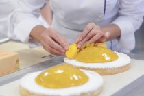 Cozinheiro feminino decorar bolos com macarons amarelos — Fotografia de Stock