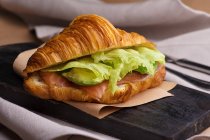 Nahaufnahme von Croissant mit Avocado und Lachsscheiben auf Teller serviert — Stockfoto