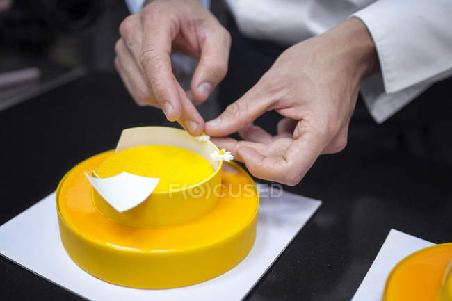 Primer plano del chef masculino que decora el pastel con caramelos de flores - foto de stock
