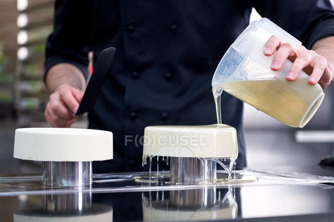 Male confectioner pouring glaze on cakes on stands — Stock Photo