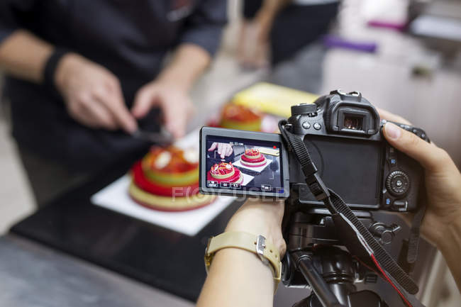 Mãos femininas segurando câmera enquanto confeiteiro fazendo bolos — Fotografia de Stock