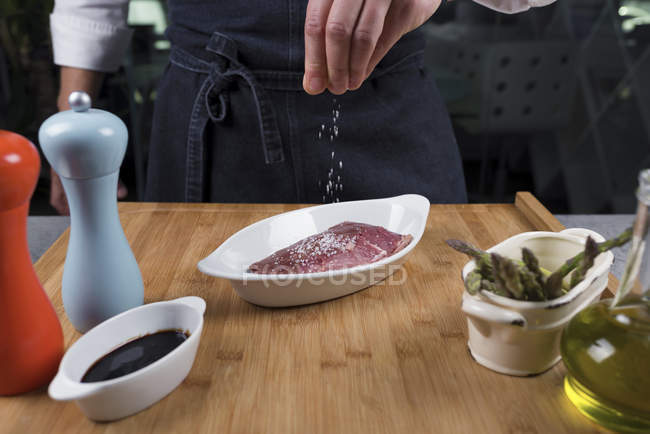 Vue rapprochée du chef salant à la main la viande — Photo de stock