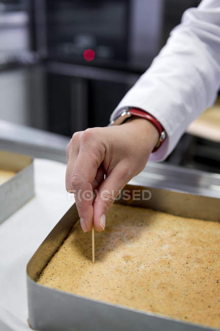 Vista cortada do chef mão verificando se o bolo é cozido — Fotografia de Stock